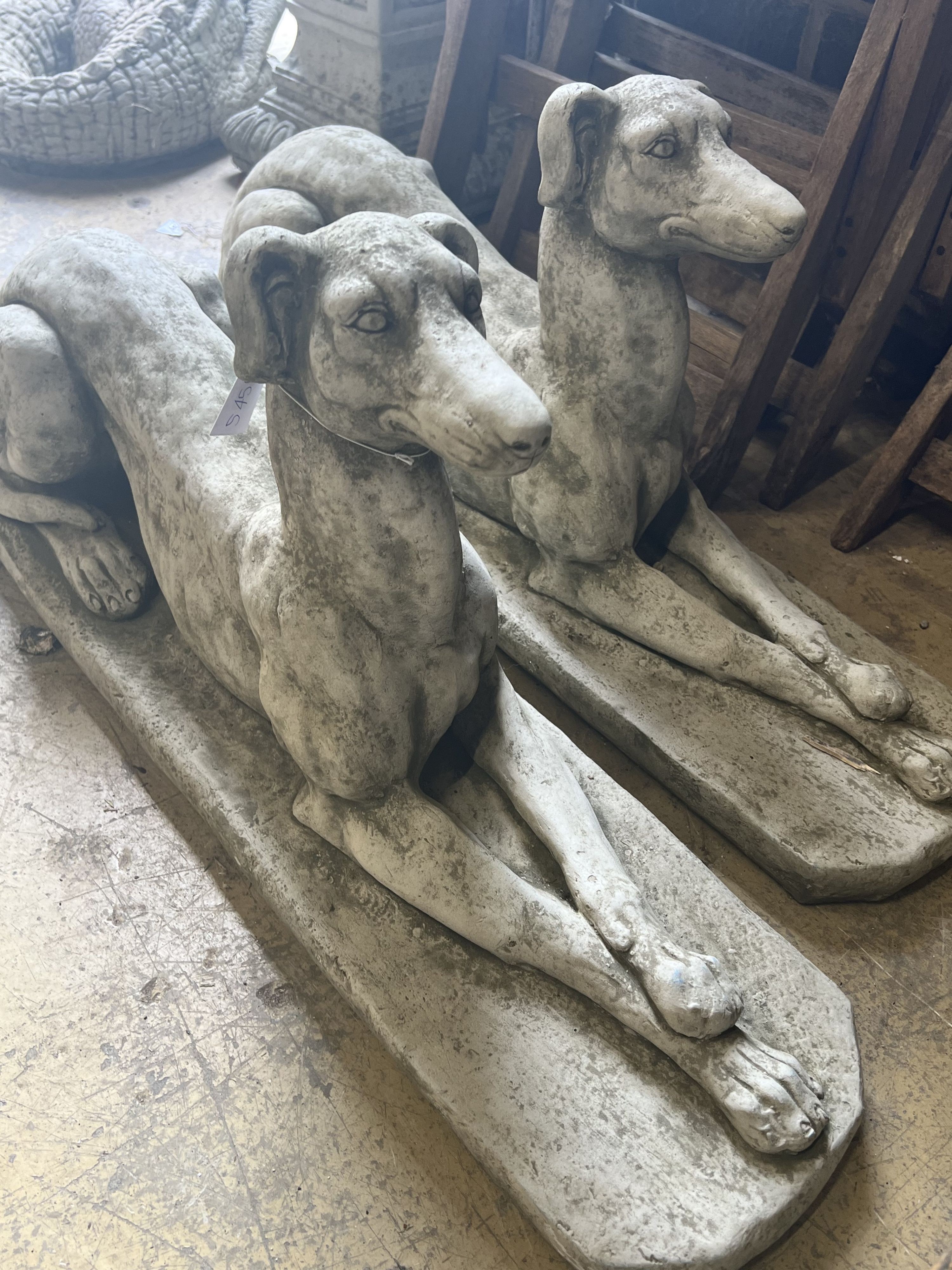 A pair of reconstituted stone recumbent greyhound ornaments, length 82cm